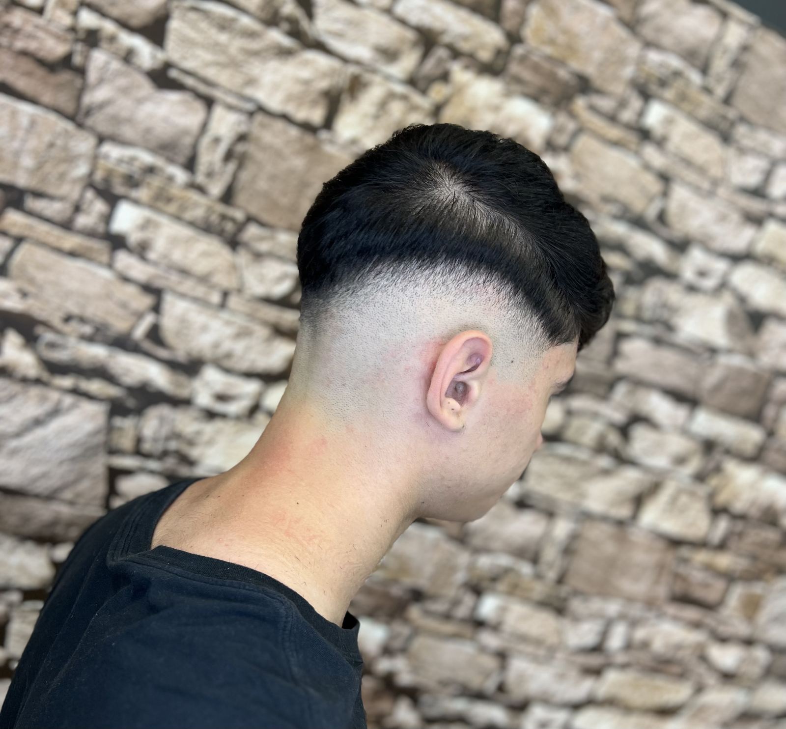 Skin fade văzut din spate, pe fundal de piatră